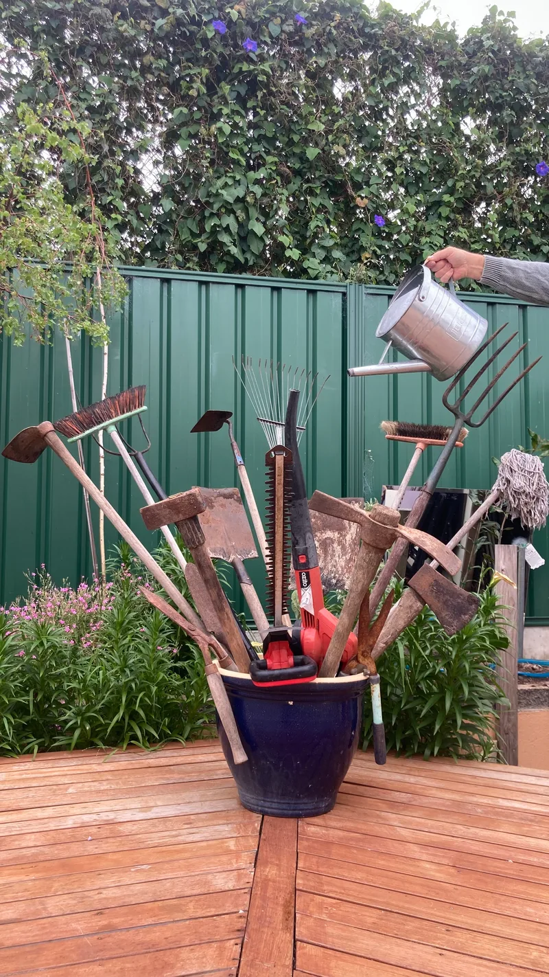 Garden tools standing in a blue pot like a bunch of flowers, watered from a can, on a timber deck